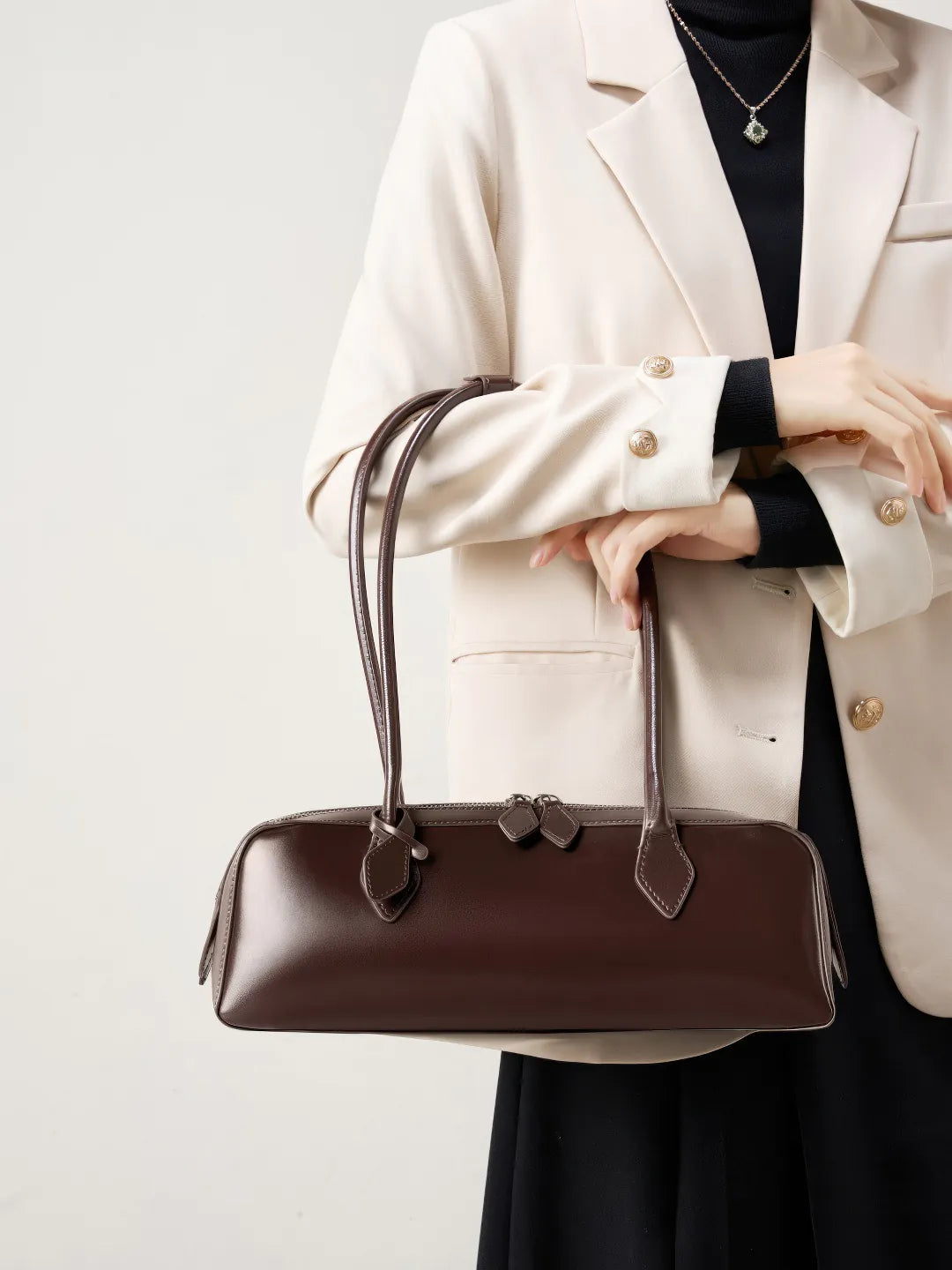 Person holding a brown leather handbag against a light background #Color_Brown