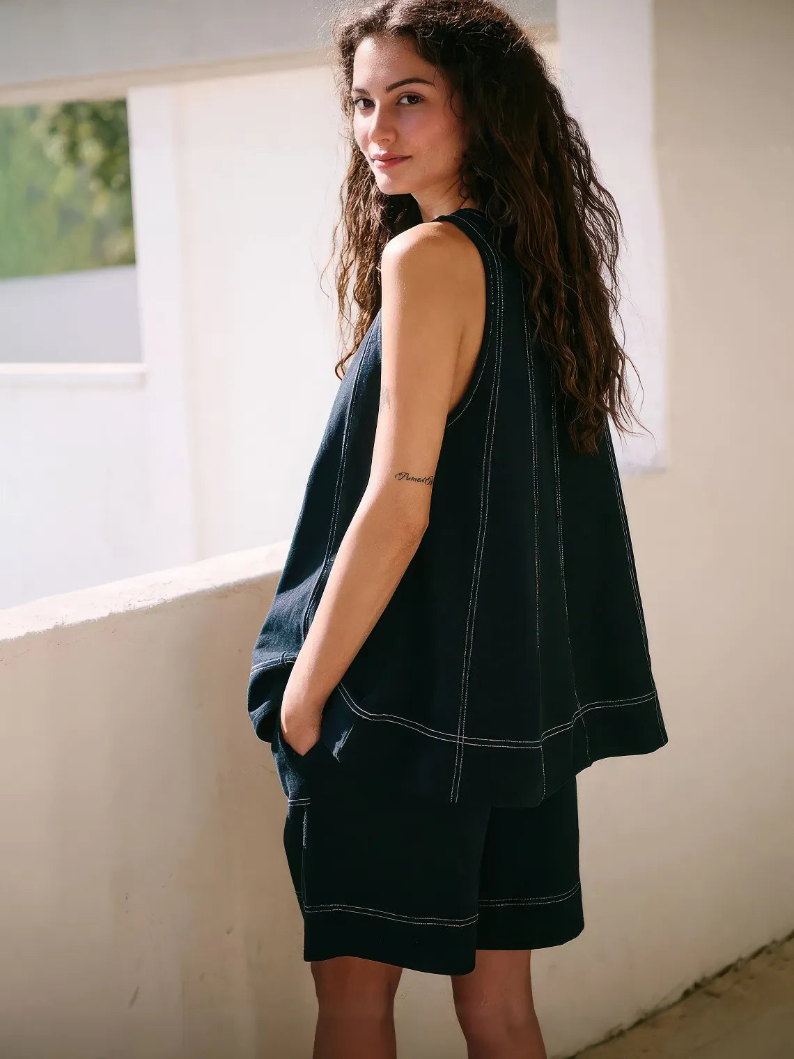 Woman wearing a dark green sleeveless top and shorts standing indoors. #Color_Black