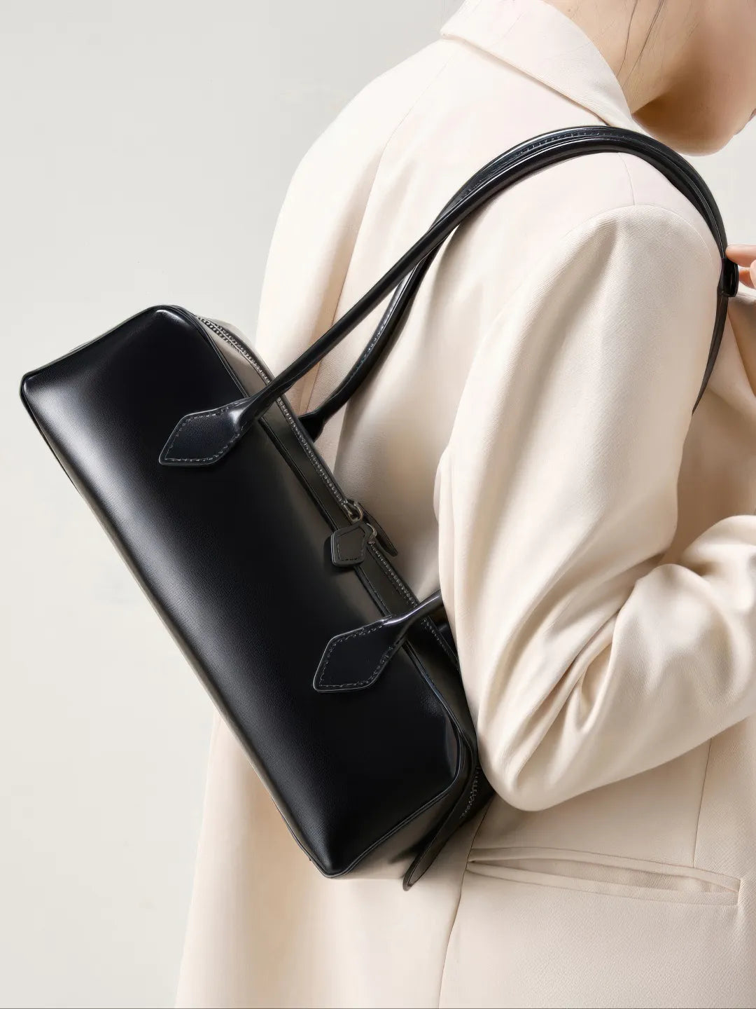 Person holding a black handbag against a neutral background #Color_Black