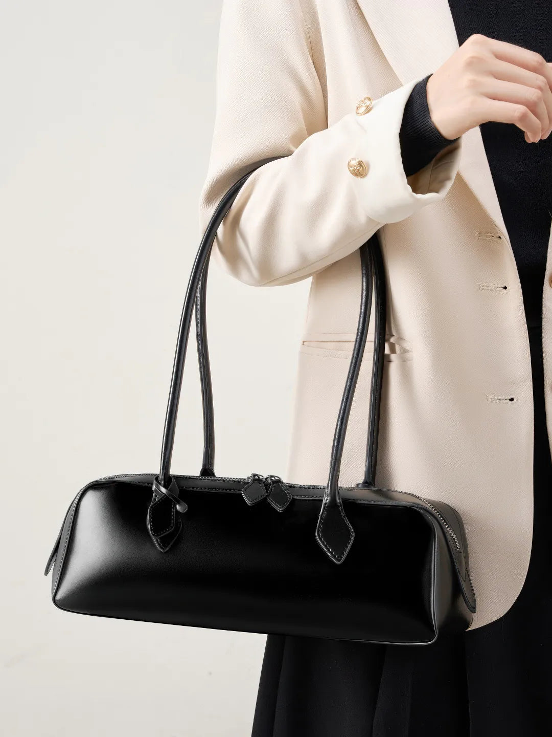 Person holding a black handbag against a neutral background #Color_Black