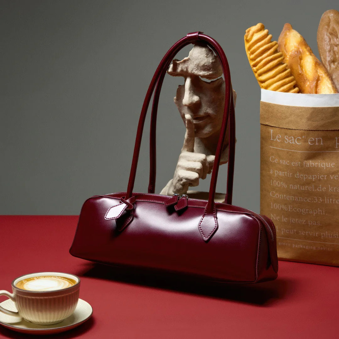 Red handbag on a red surface with a cup of coffee, bag of fries, and sculpture in the background. #Color_Red