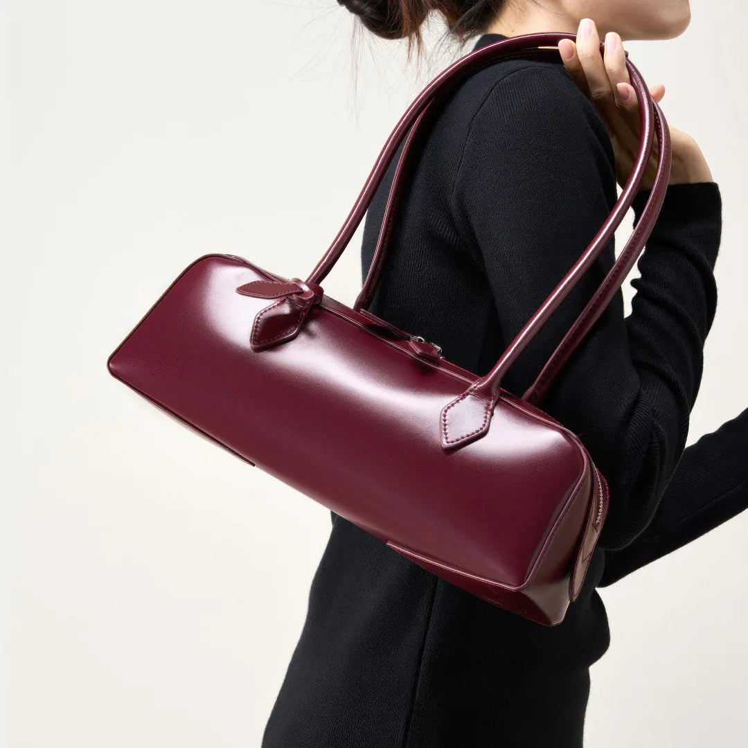 Person holding a burgundy handbag against a neutral background #Color_Red