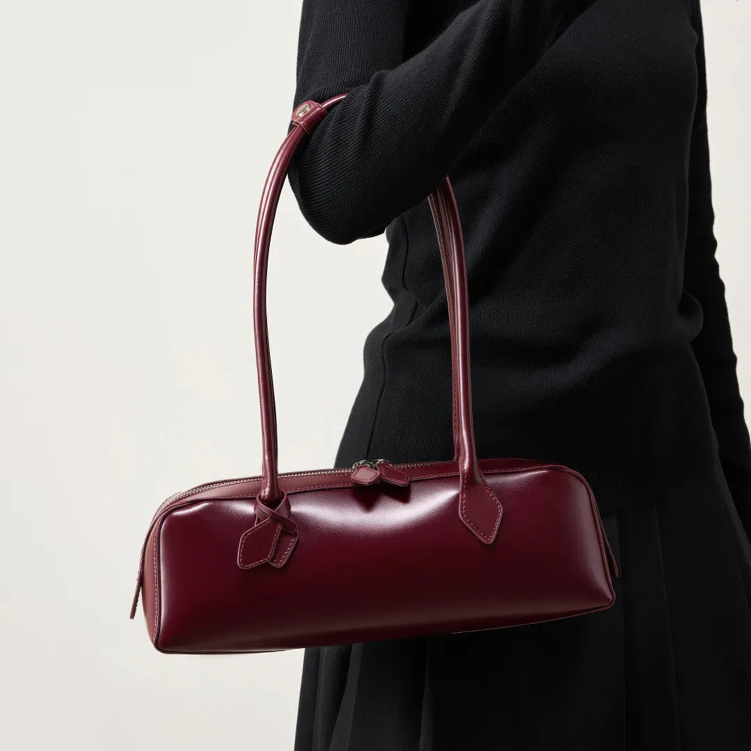 Burgundy handbag held by a person wearing a black coat on a light background #Color_Red