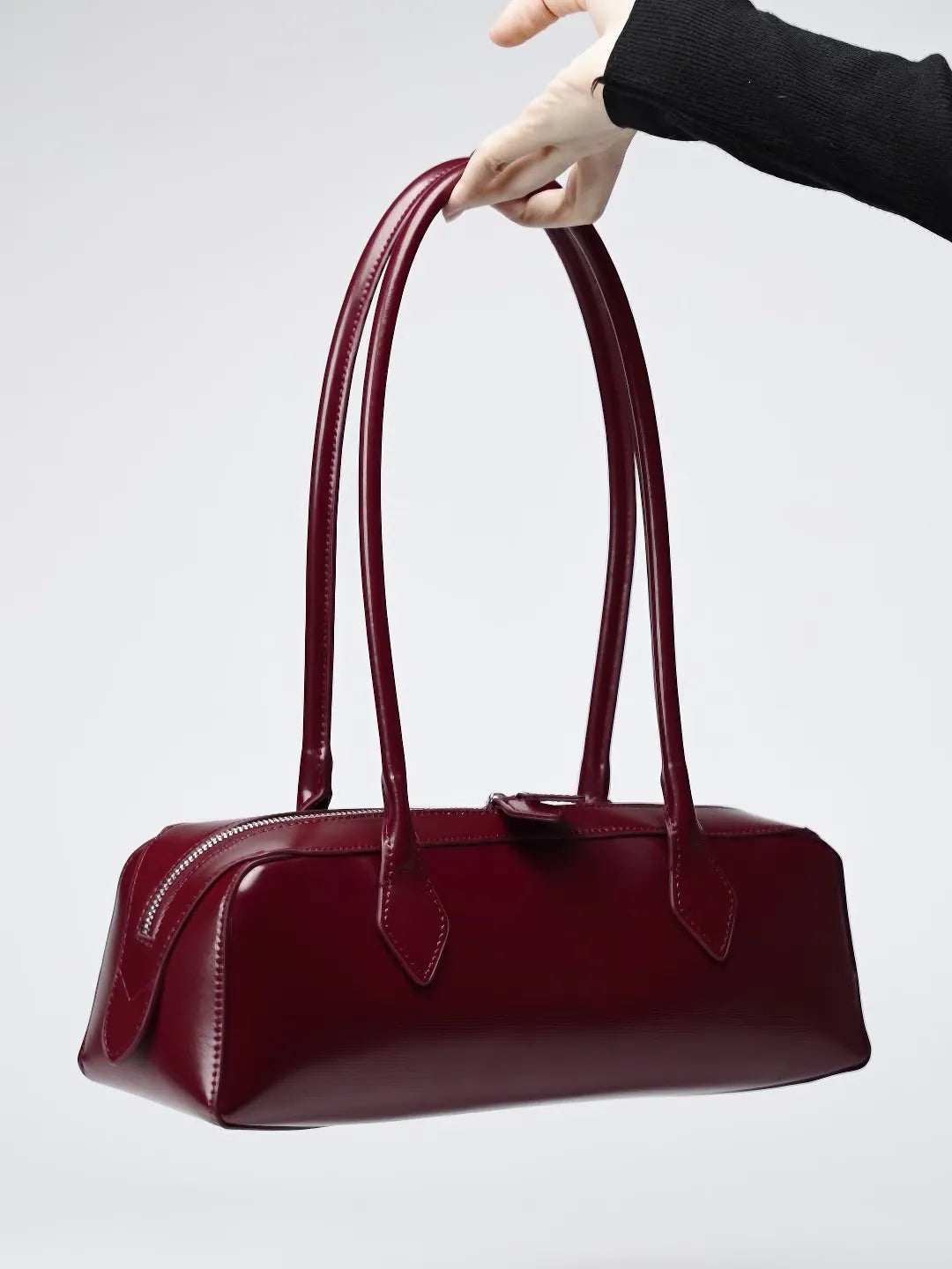 Burgundy handbag held by a hand against a light gray background #Color_Red