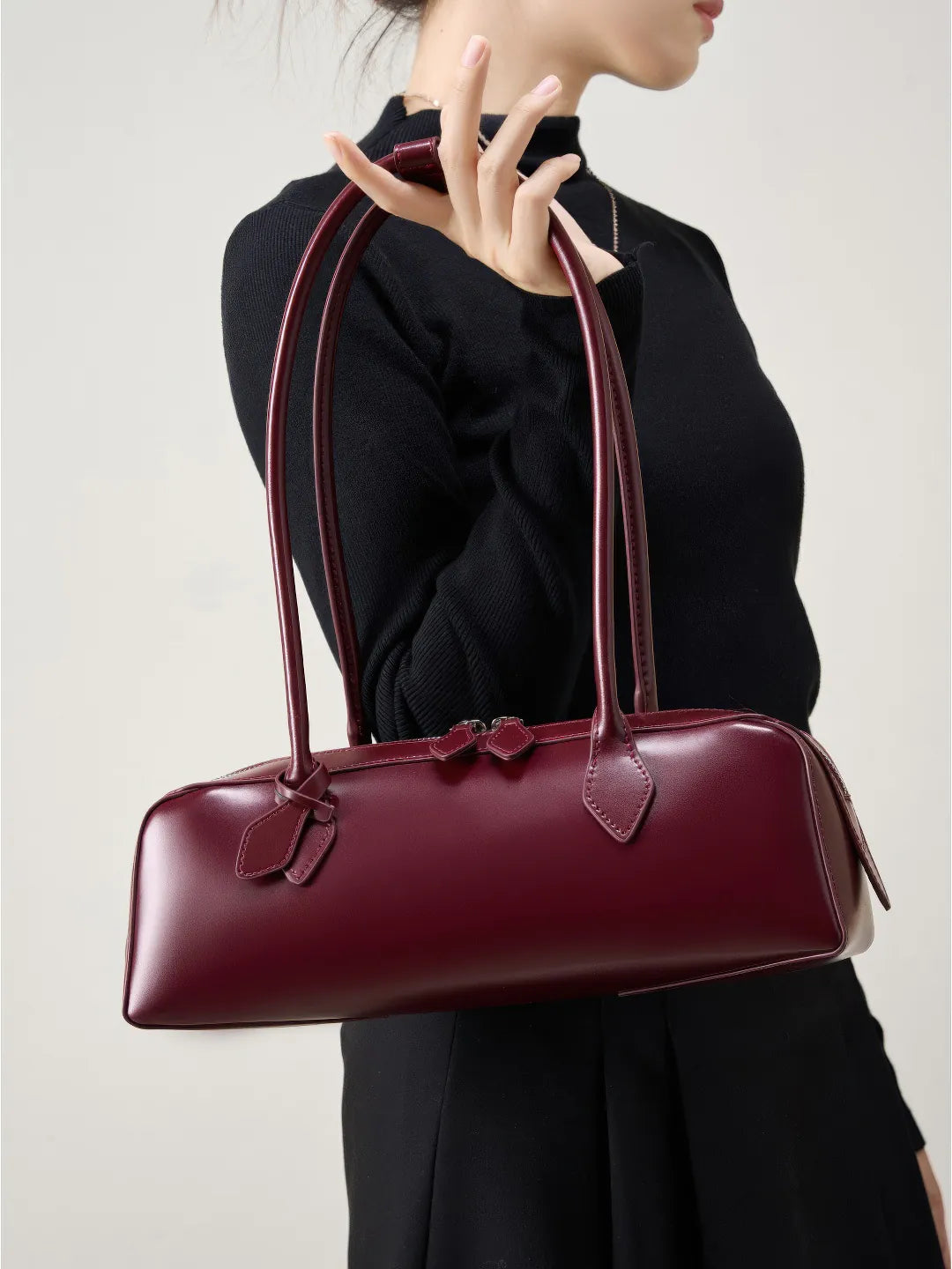 Burgundy handbag held by a person wearing a black outfit on a light background #Color_Red