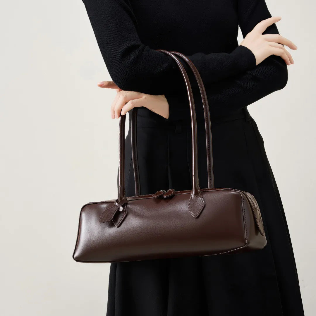 Person holding a brown leather handbag against a plain background #Color_Brown