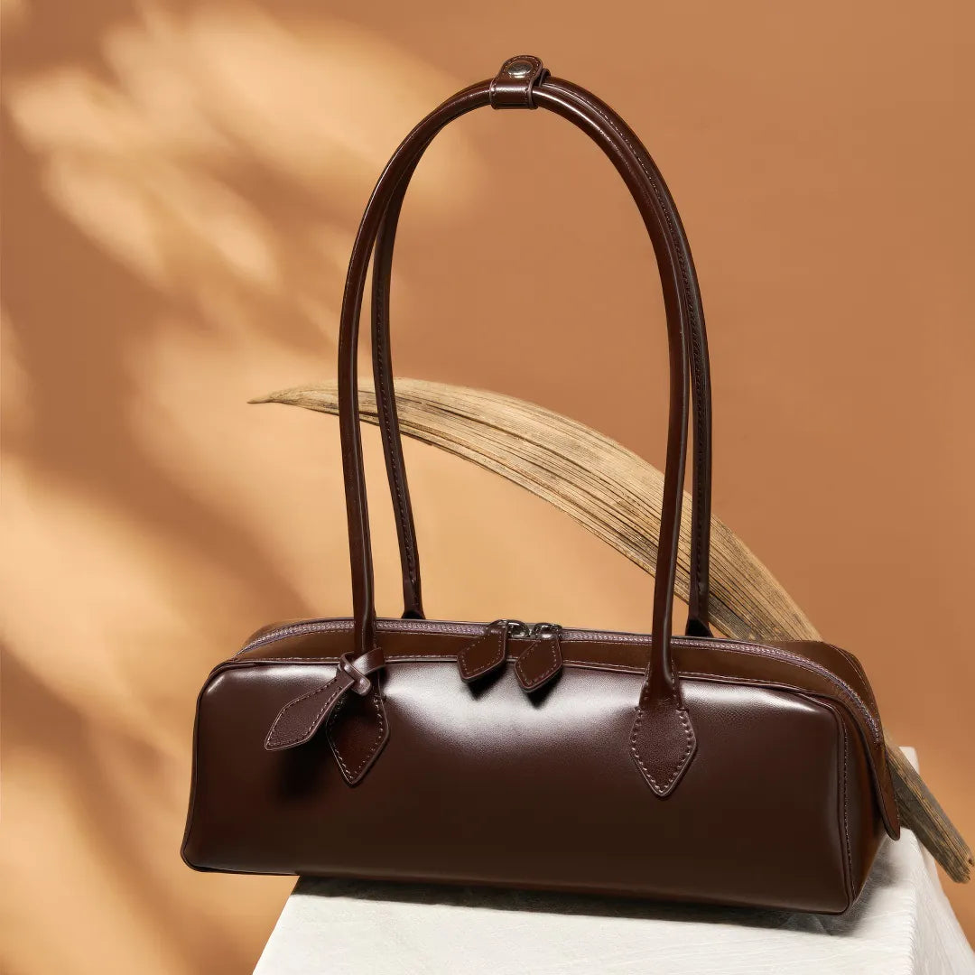 Brown leather handbag with bow details on a wooden surface and leaf background #Color_Brown