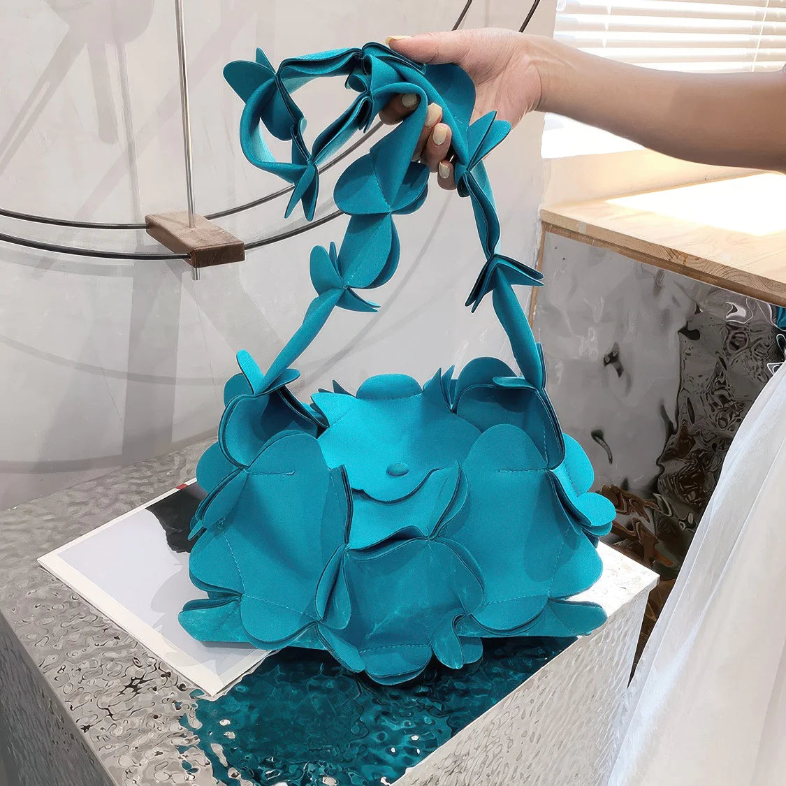 Turquoise handbag with floral design held by a person indoors. #Color_Teal