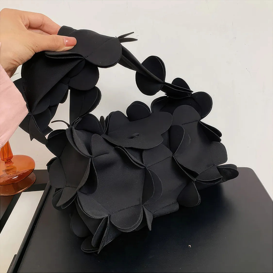 Black paper flower headband being adjusted by a hand on a white background. #Color_Black