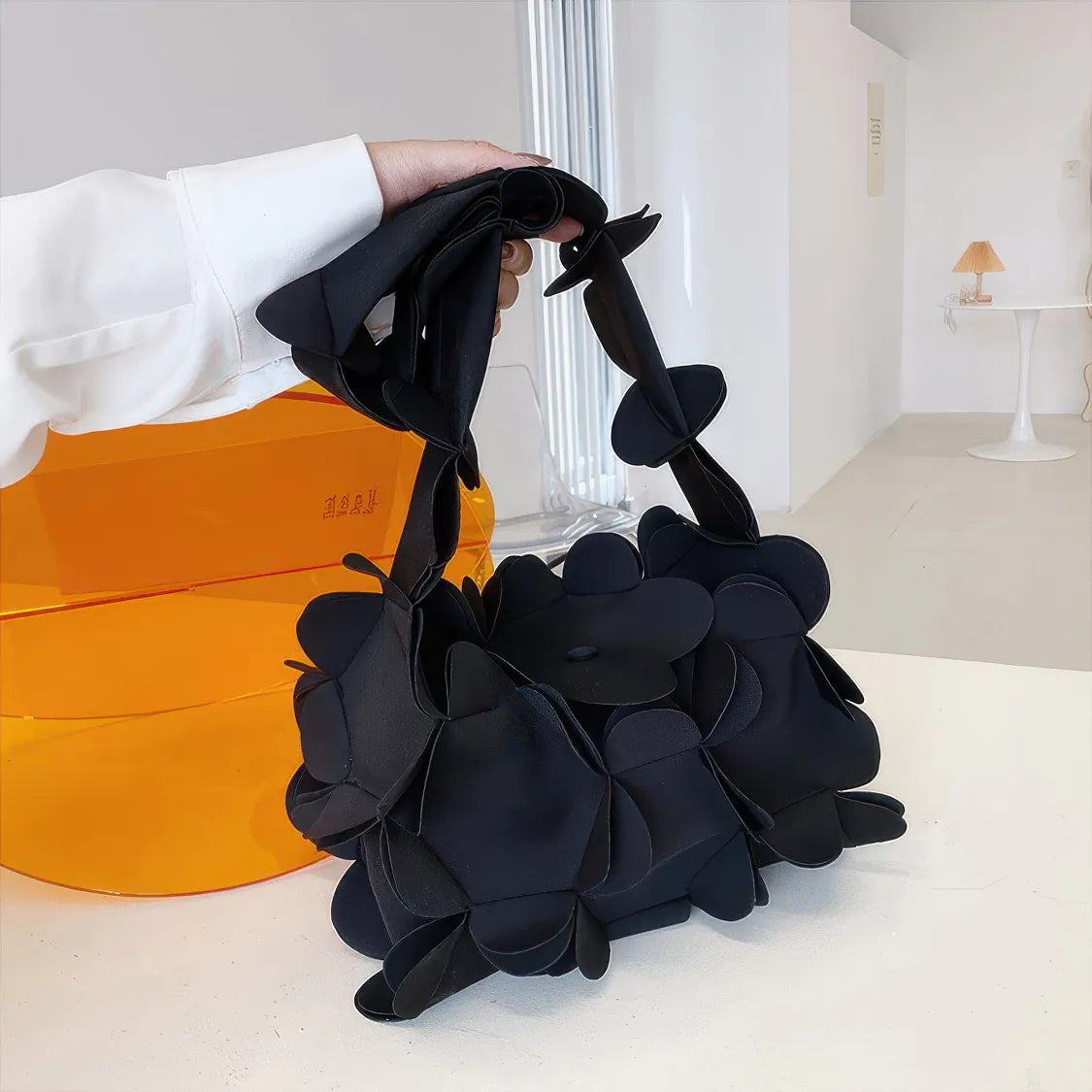 Black floral handbag held by a person with an orange box in the background. #Color_Black