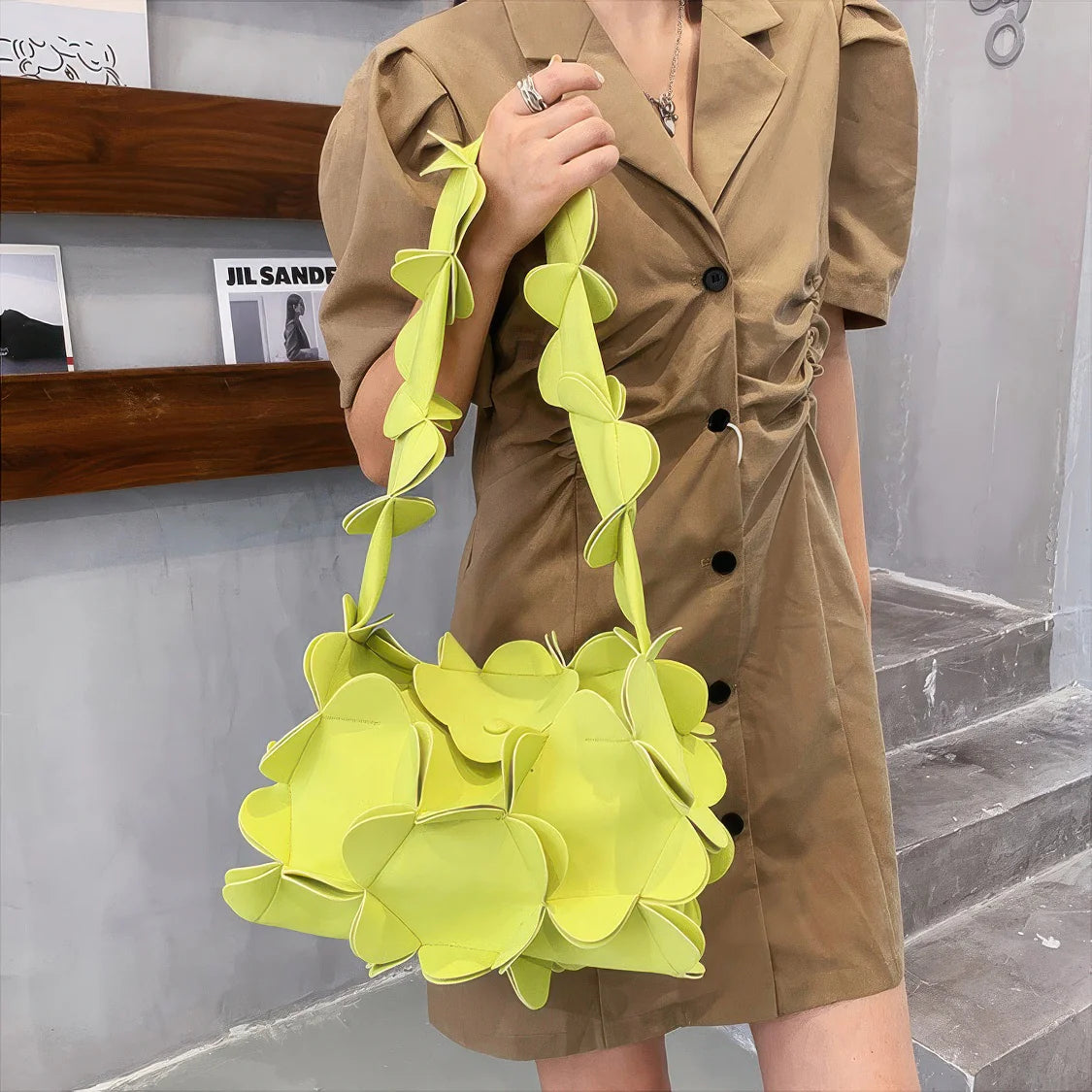 Person holding a bright yellow floral handbag wearing a beige trench coat. #Color_Green