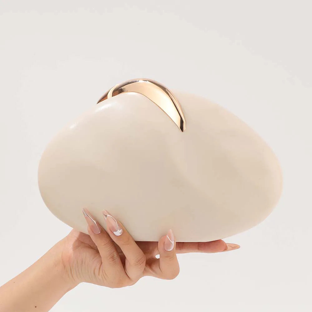 Beige clutch with gold accent held by a hand on a light gray background. #Color_Beige