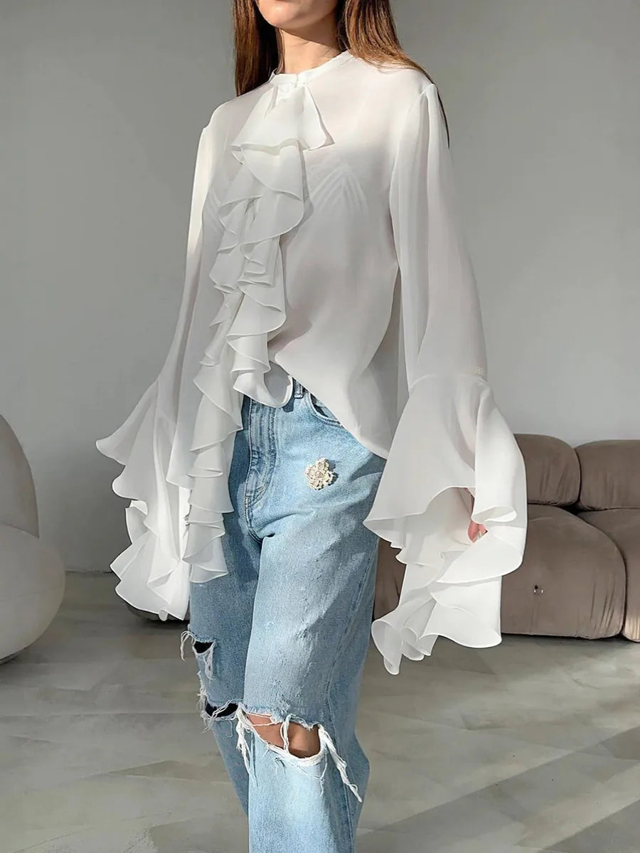 Person wearing a white ruffled blouse and light blue jeans in a minimalistic room. #Color_White