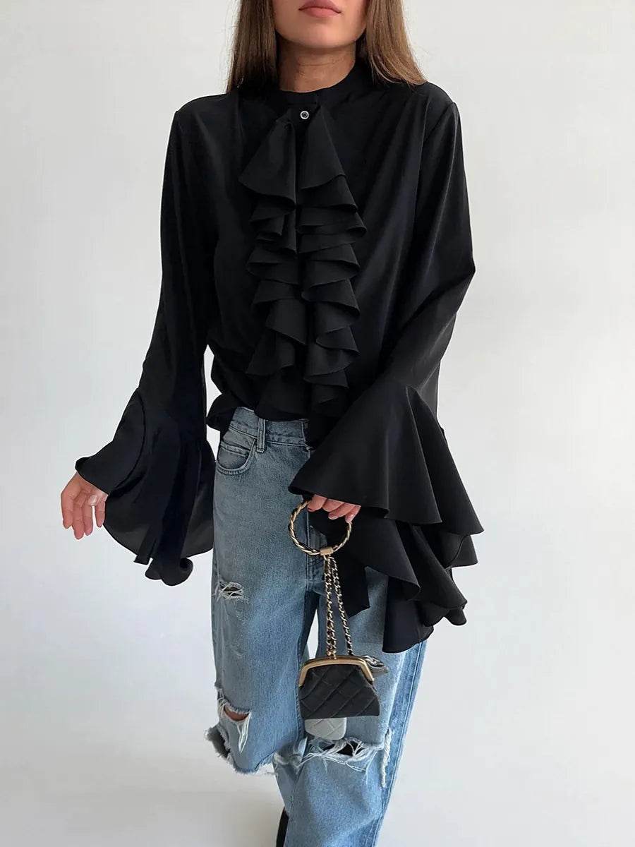 Person wearing a black ruffled blouse and blue jeans, holding a black handbag against a white background  #Color_Black