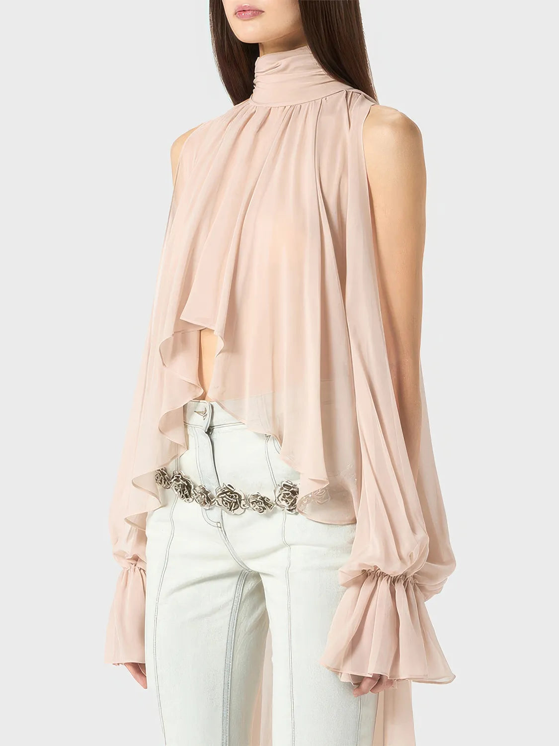 Woman wearing a light pink blouse with sheer sleeves and white pants on a plain background. #Color_Pink