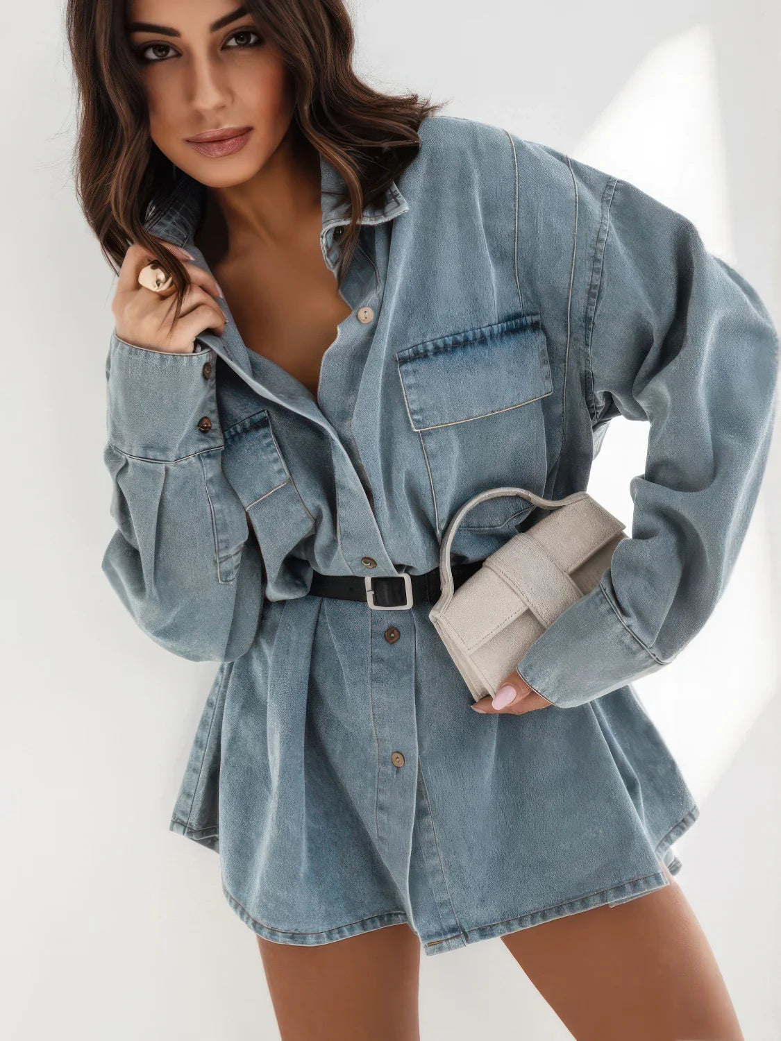 Woman wearing a denim outfit holding a beige handbag on a white background