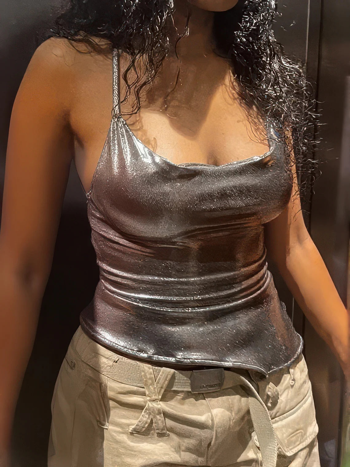 Person wearing a shiny silver tank top and beige pants against a dark background
