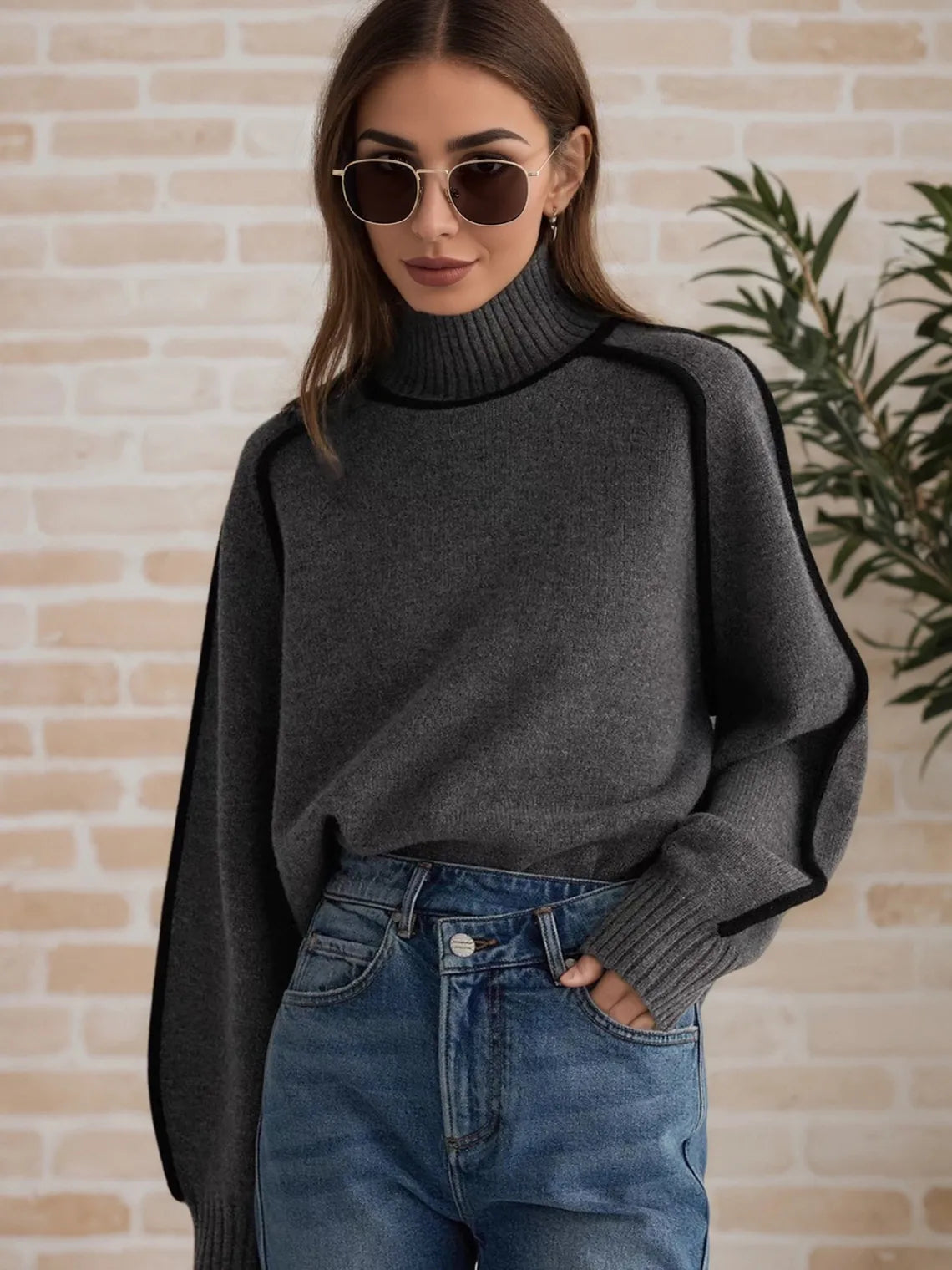 Woman wearing a dark gray sweater and blue jeans against a brick wall. #Color_DimGray