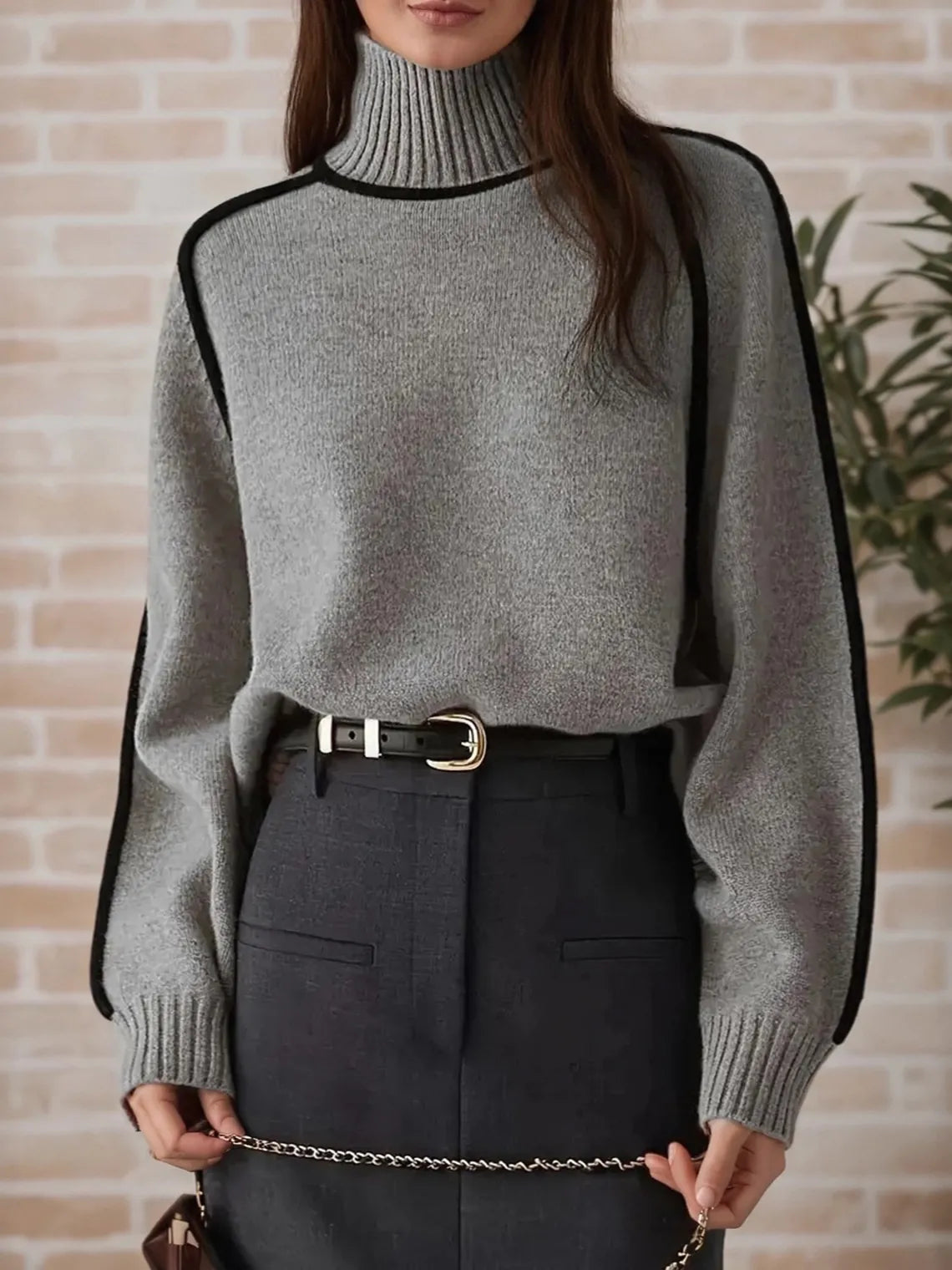 Person wearing a gray sweater with black accents against a brick wall. #Color_Gray