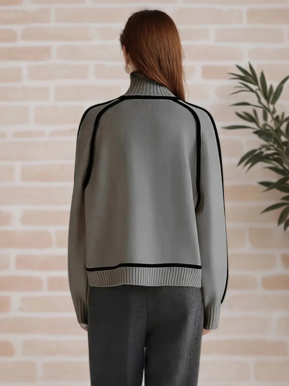 Person wearing a gray sweater with black accents against a brick wall. #Color_Gray