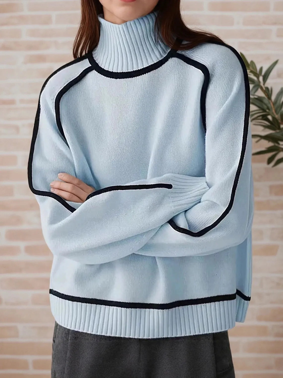 Light blue sweater with black trim worn by a person against a beige wall. #Color_LightBlue