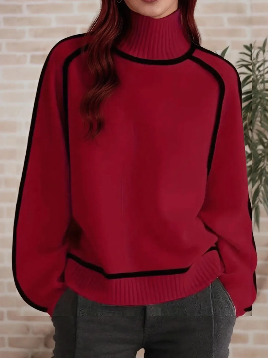 Person wearing a red sweater with black trim against a beige wall. #Color_DarkGed