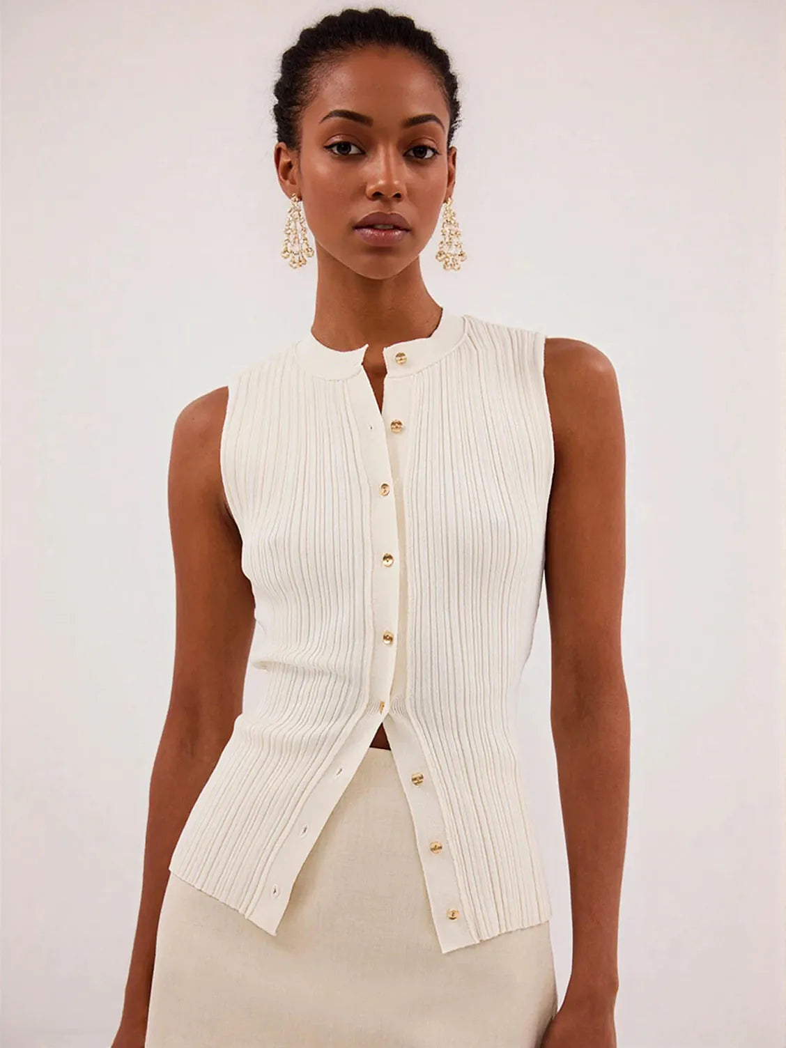 Woman wearing a white ribbed vest with gold buttons against a plain background. #Color_Beige