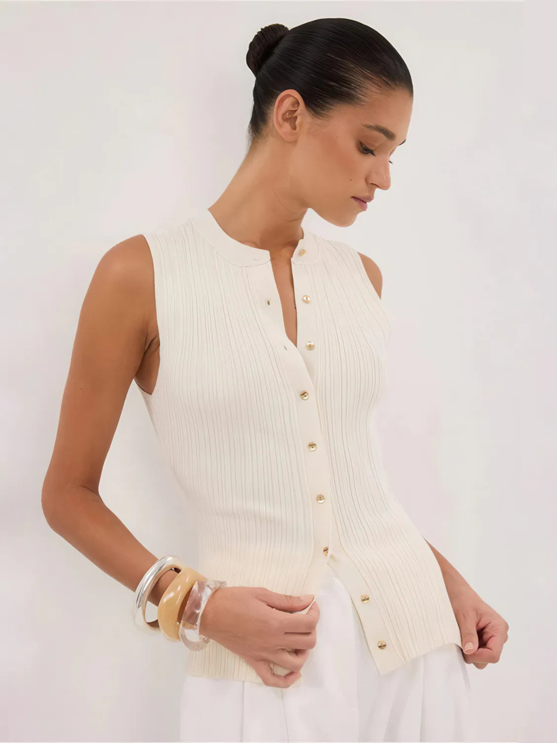 Woman wearing a cream-colored sleeveless button-up top against a white background. #Color_Beige