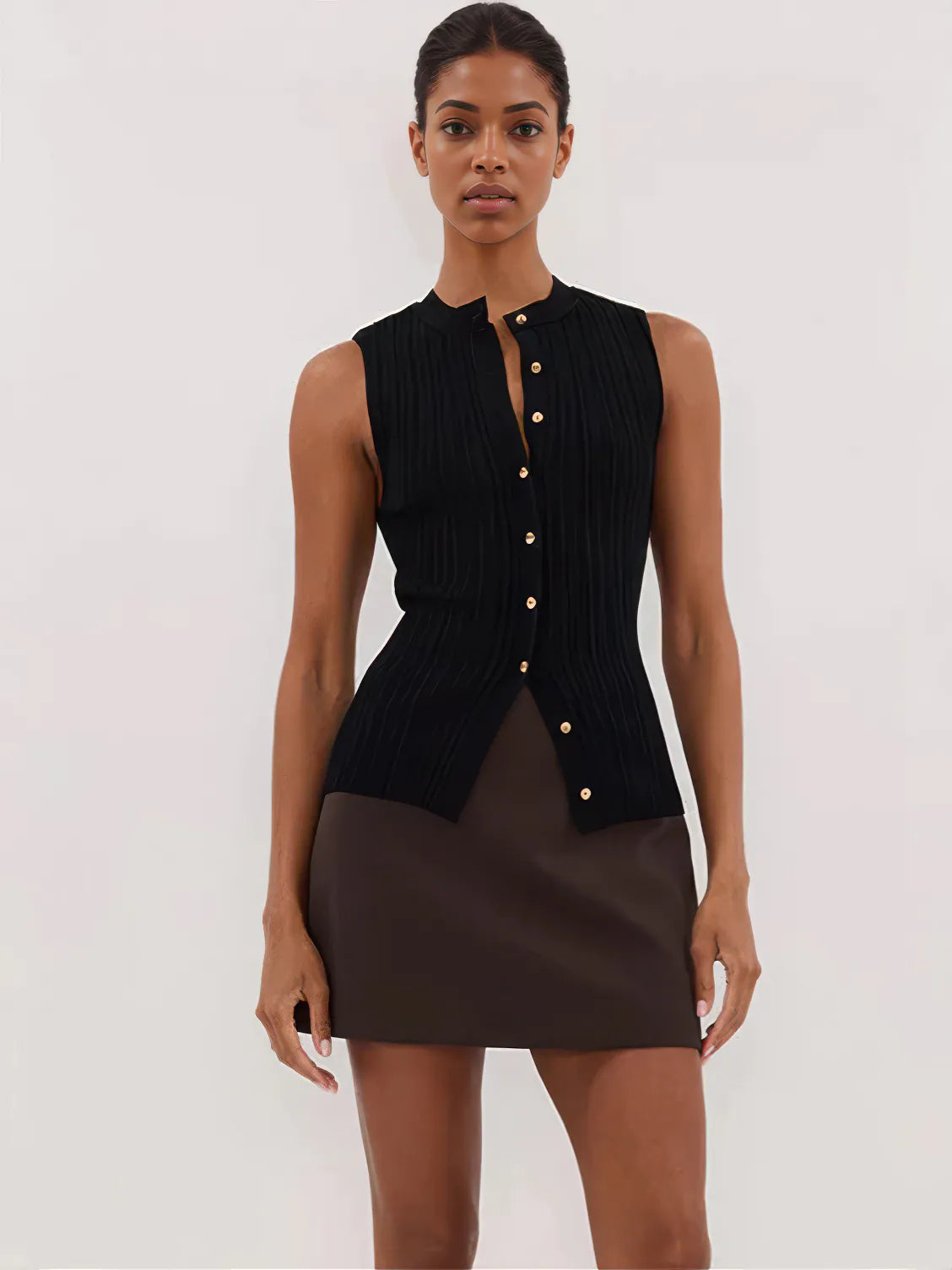 Woman wearing a black sleeveless top with gold buttons and a brown skirt on a white background. #Color_Black