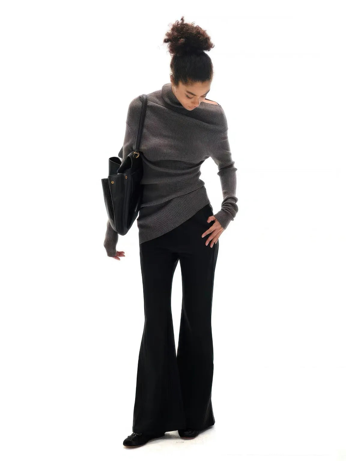 Woman wearing a gray sweater and black pants holding a black handbag on a white background.#Color_Gray