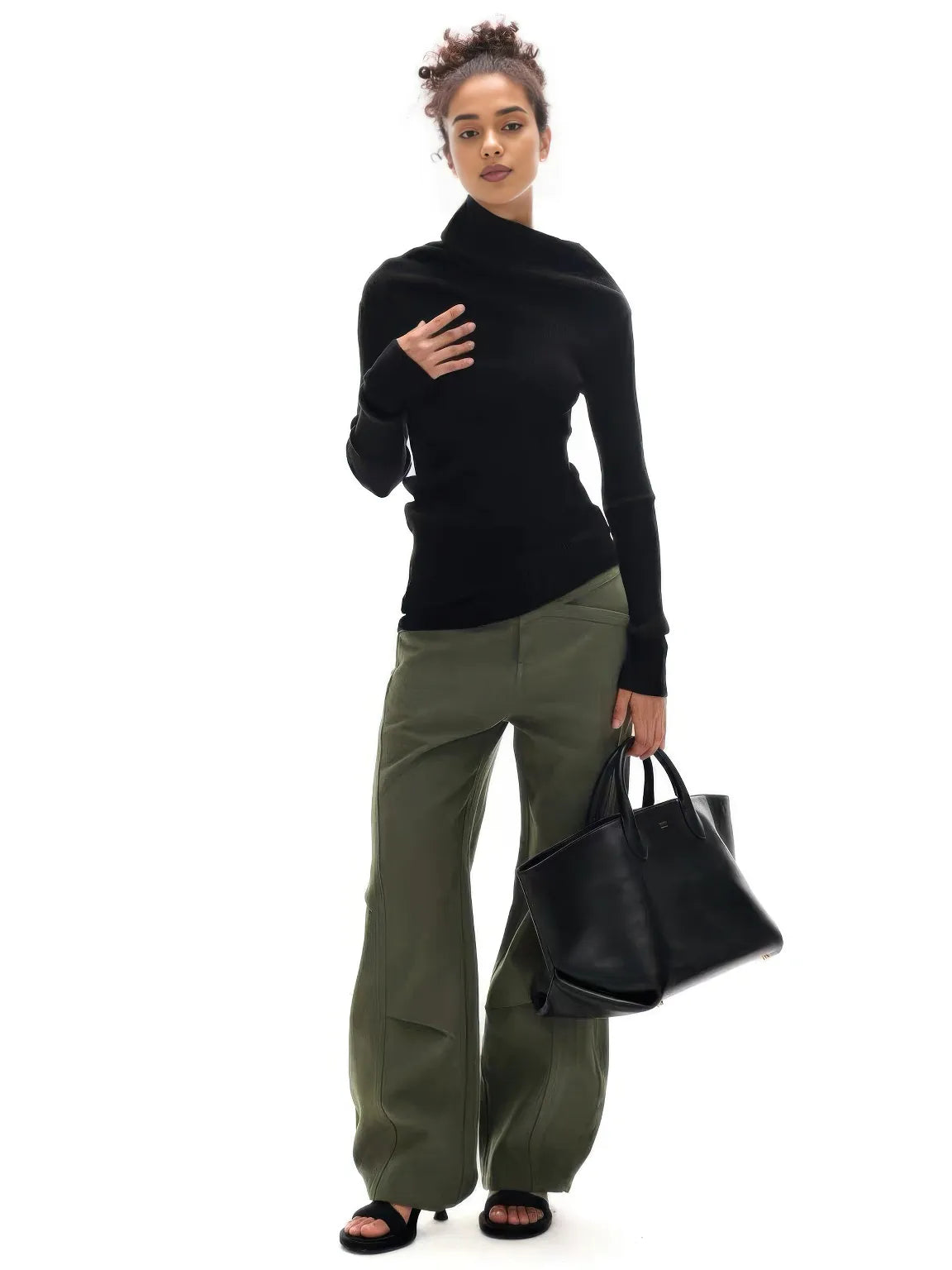 Woman wearing a black turtleneck and green pants, holding a black handbag on a white background.#Color_Black