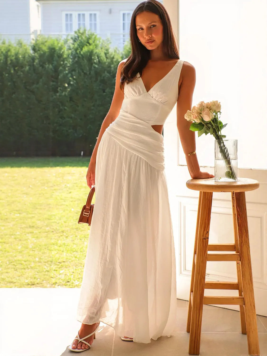 Woman in a white dress standing next to a wooden stool with flowers in an outdoor setting #Color_White