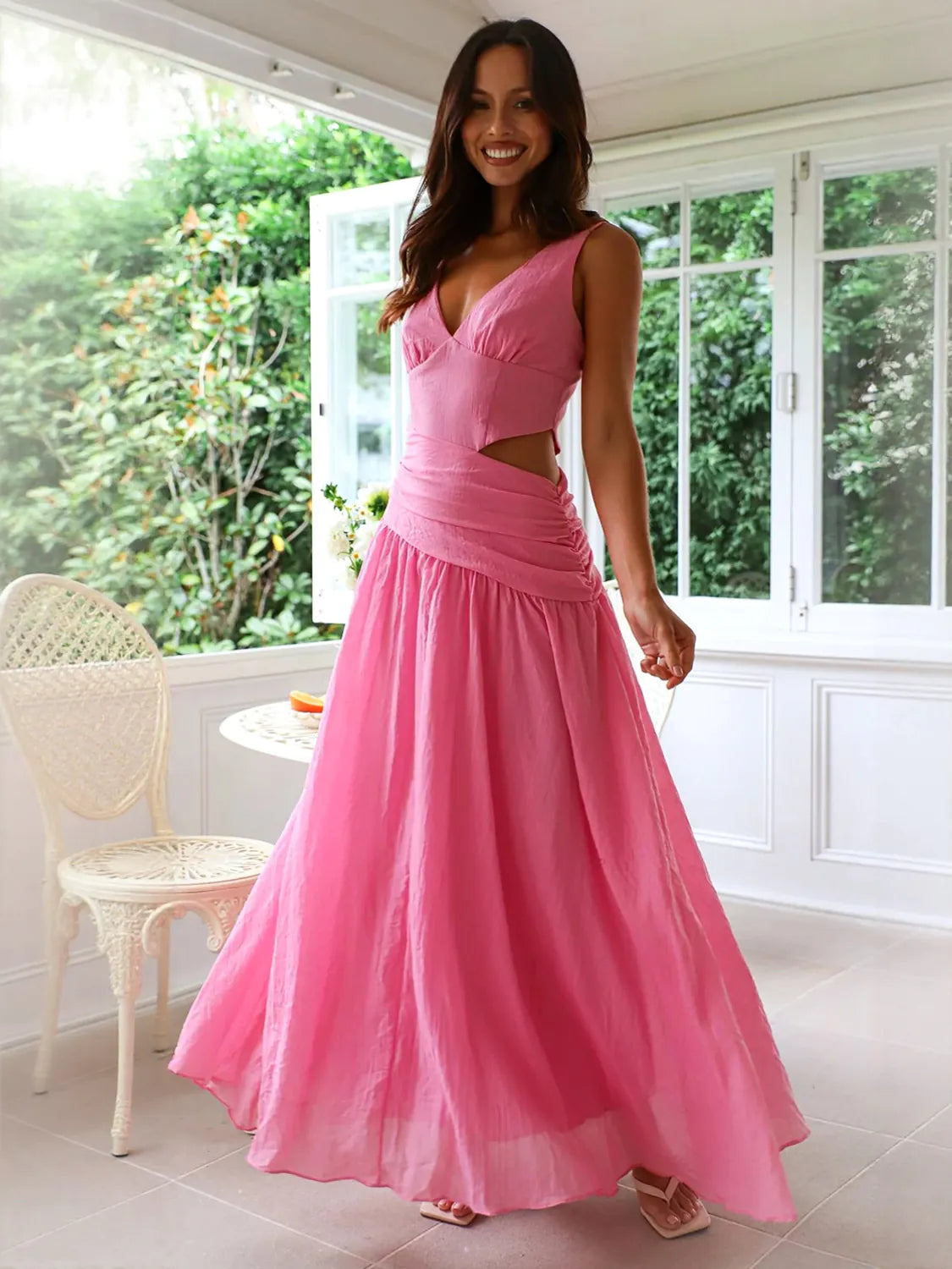 Woman wearing a pink dress standing in a room with white walls and a window. #Color_HotPink