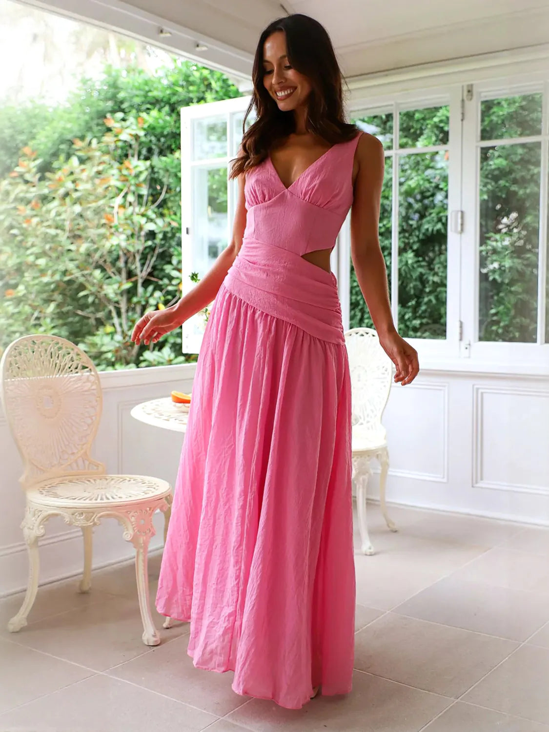 Woman wearing a pink dress standing in a bright room with white walls and a window. #Color_HotPink