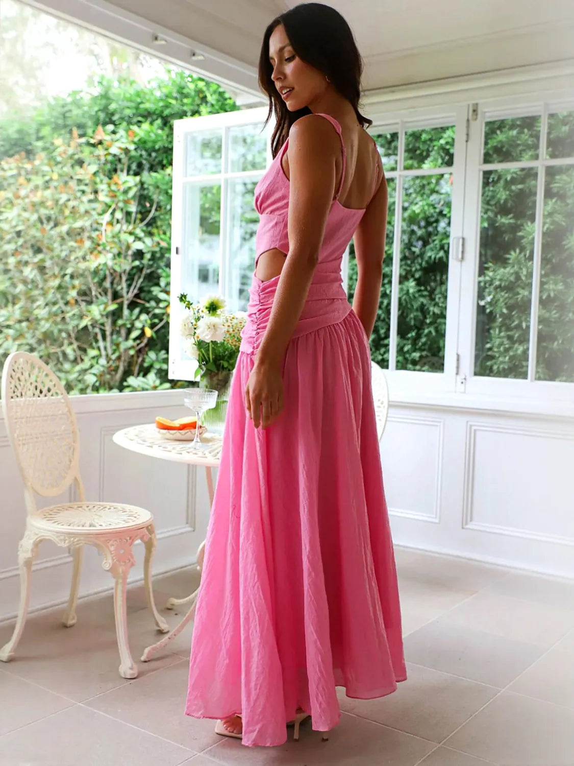 Woman in a pink dress standing in a sunroom with large windows and white furniture. #Color_HotPink