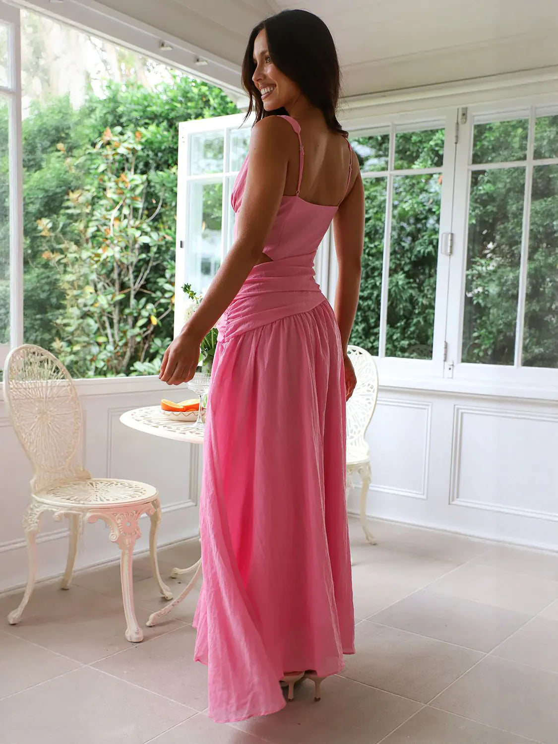 Woman in a pink dress standing in a sunroom with large windows. #Color_HotPink