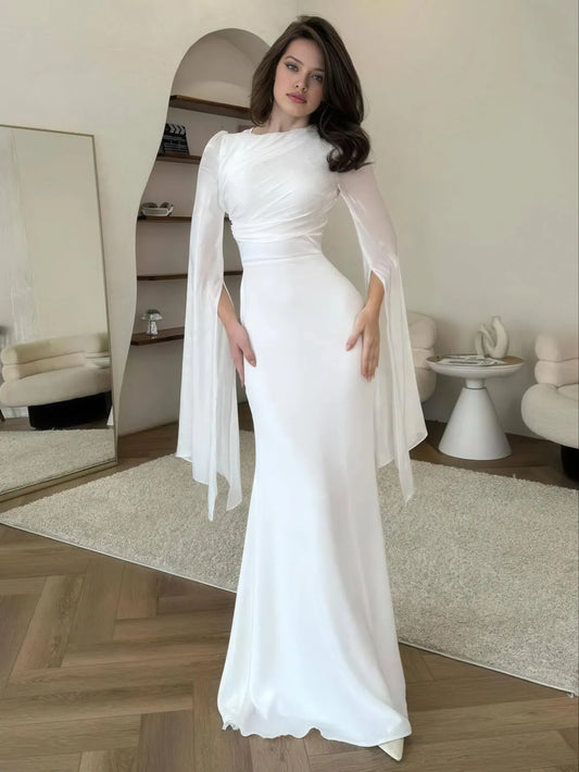 Woman in a white dress with cape in a room with a mirror and furniture. #Color_White