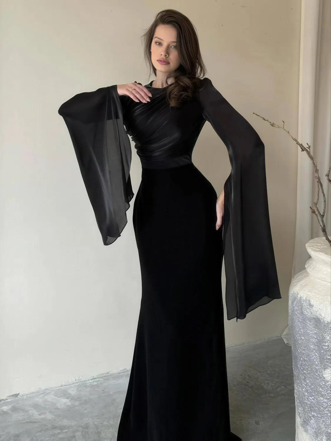 Woman wearing a black dress with wide sleeves in an indoor setting. #Color_Black