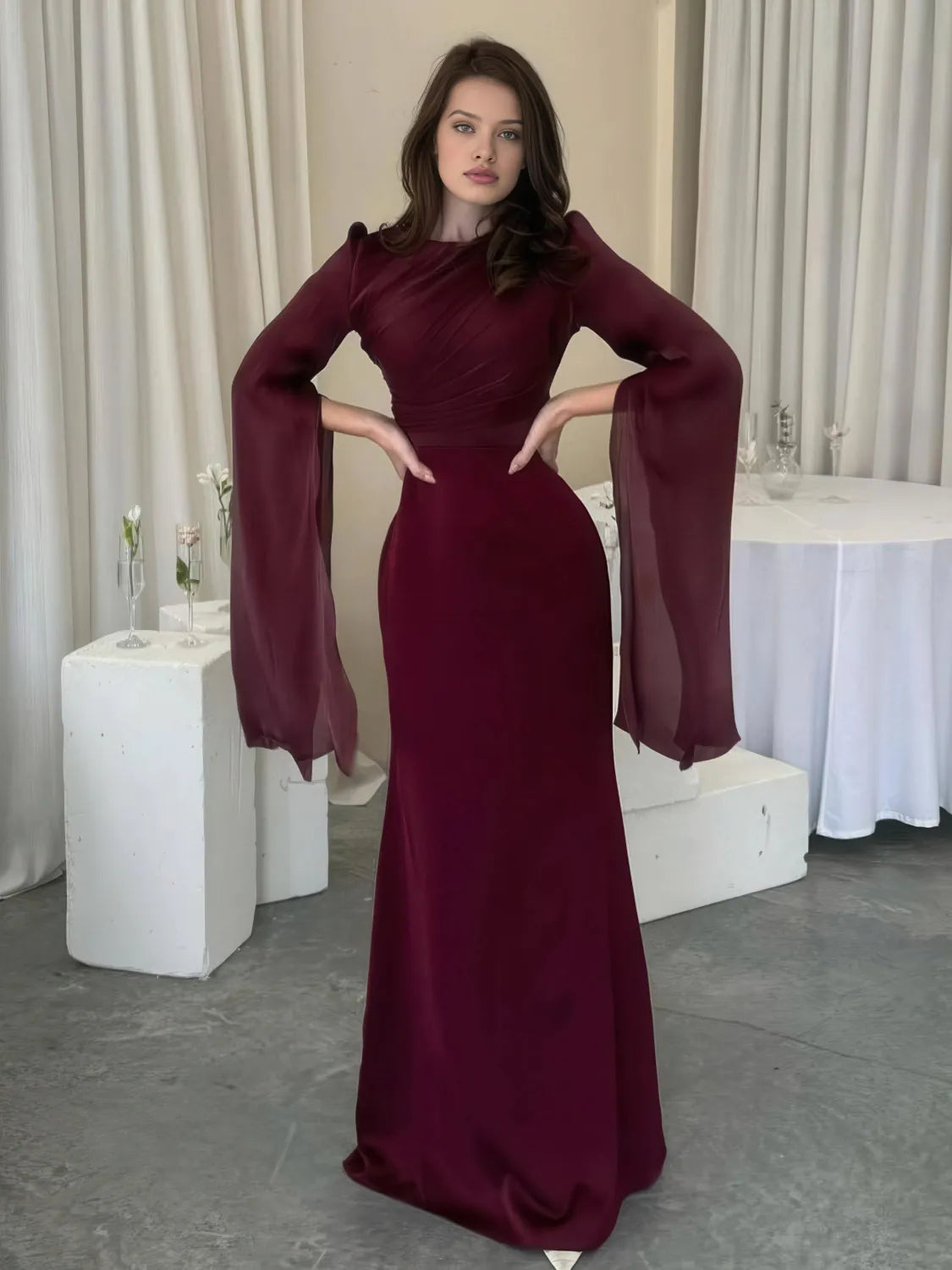 Woman in a burgundy evening gown with wide sleeves in an indoor setting. #Color_Red