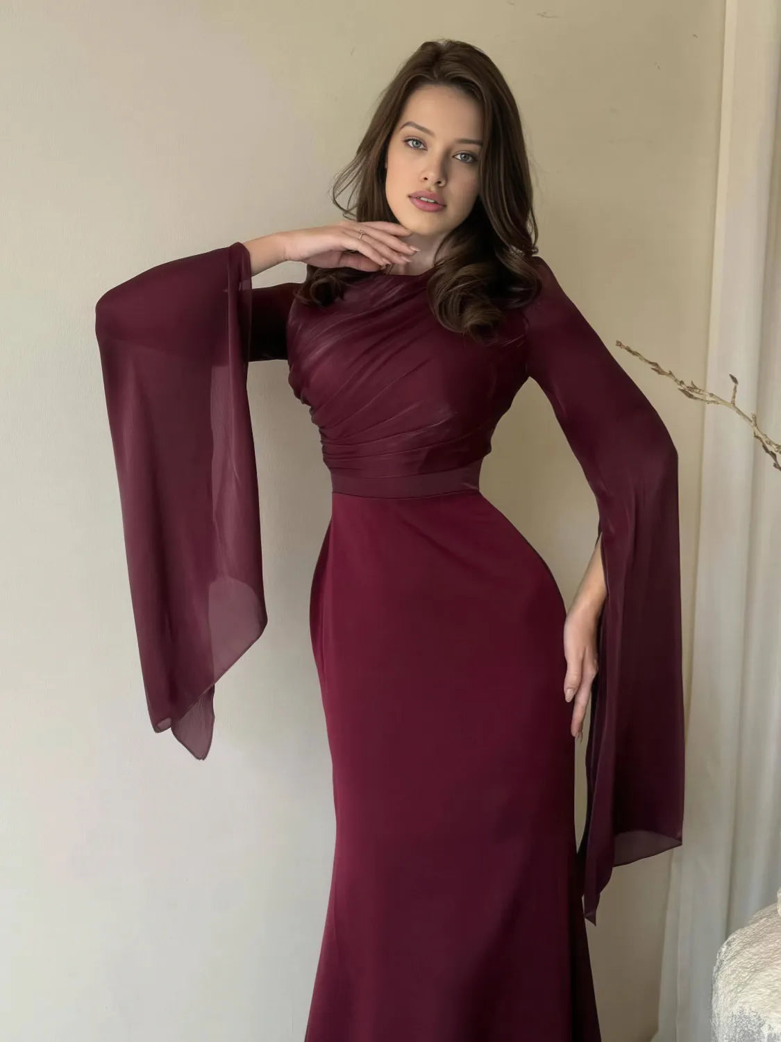 Woman wearing a burgundy evening gown with sheer sleeves against a neutral background. #Color_Red