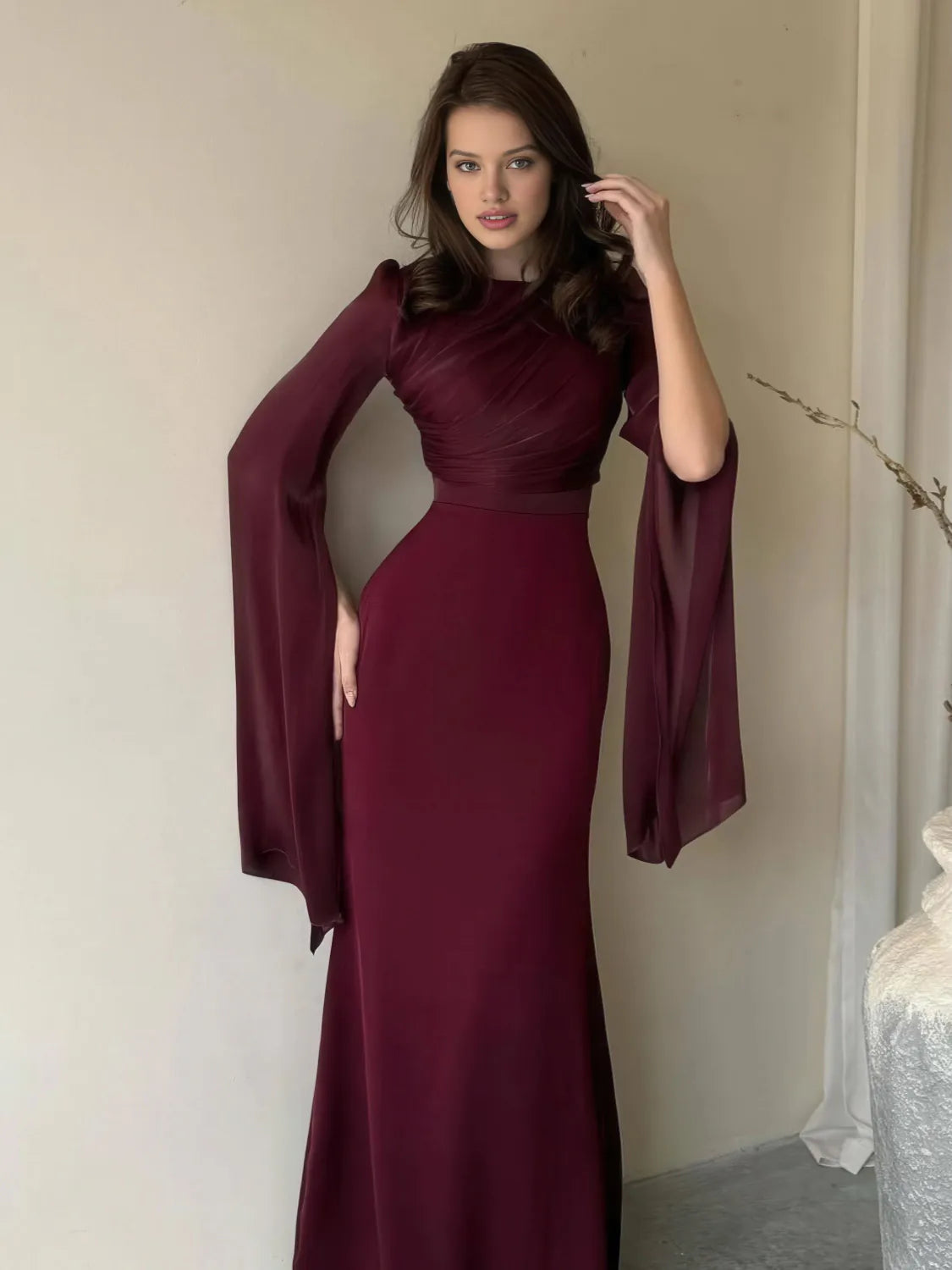 Woman wearing a burgundy evening gown with long sleeves against a neutral background. #Color_Red