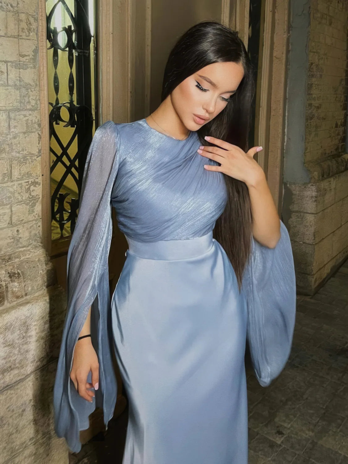 Woman in a light blue dress standing against a stone wall. #Color_Blue
