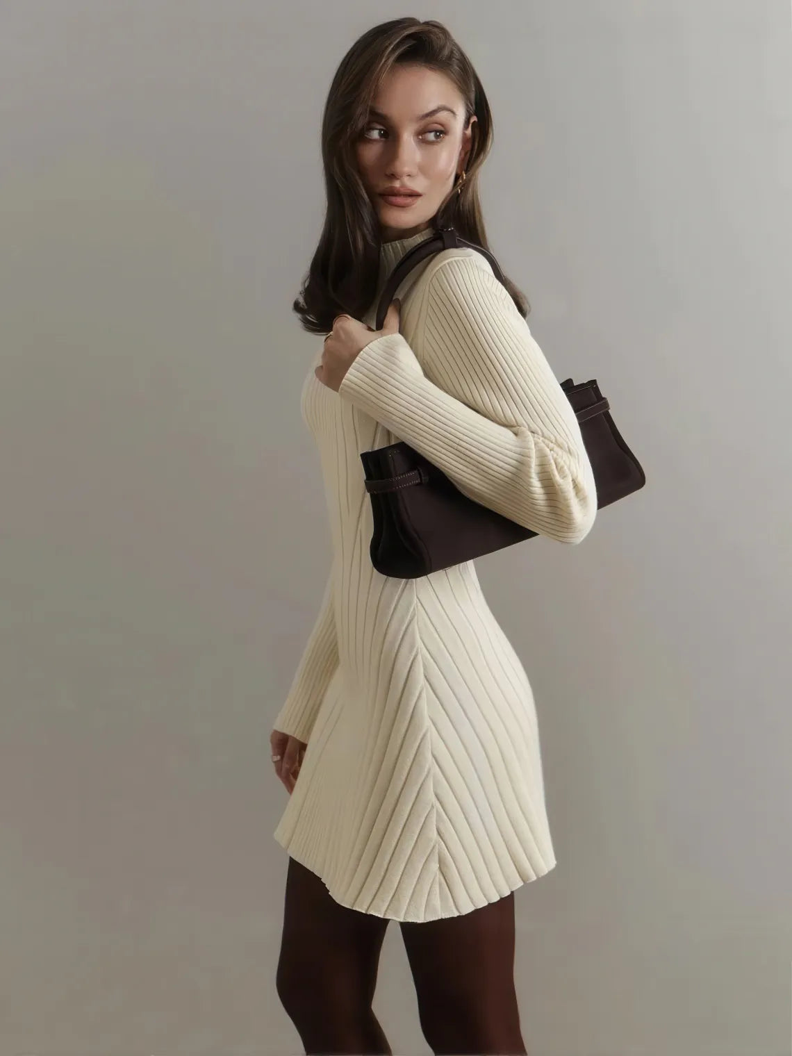 Woman wearing a white ribbed sweater dress holding a black handbag against a plain background. #Color_Beige