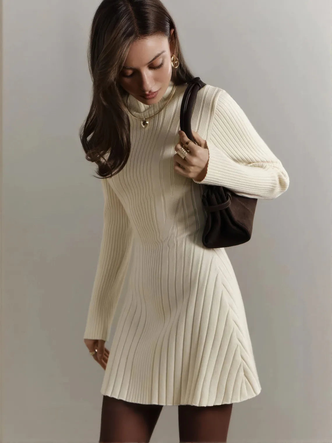 Woman wearing a cream ribbed dress holding a brown handbag against a plain background. #Color_Beige