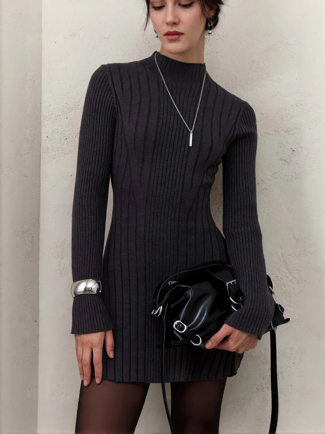 Woman wearing a black ribbed dress holding a black handbag against a neutral background. #Color_Black