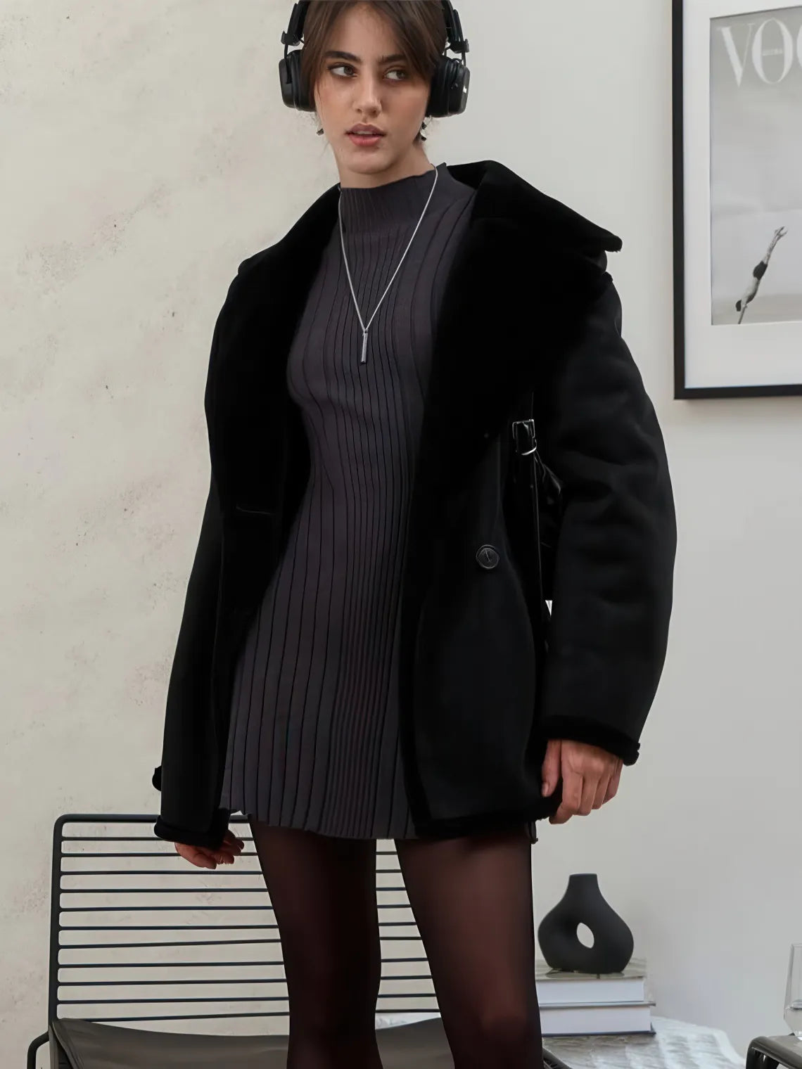 Woman wearing a black coat over a dark dress with headphones, standing indoors. #Color_Black