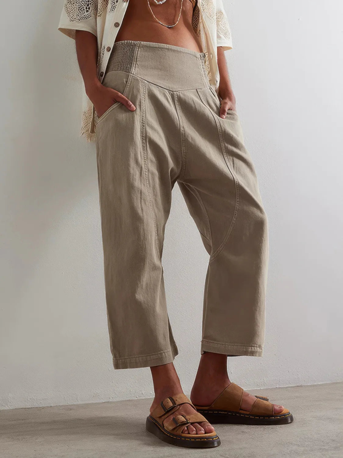 Person wearing beige pants and sandals against a plain background. #Color_Tan