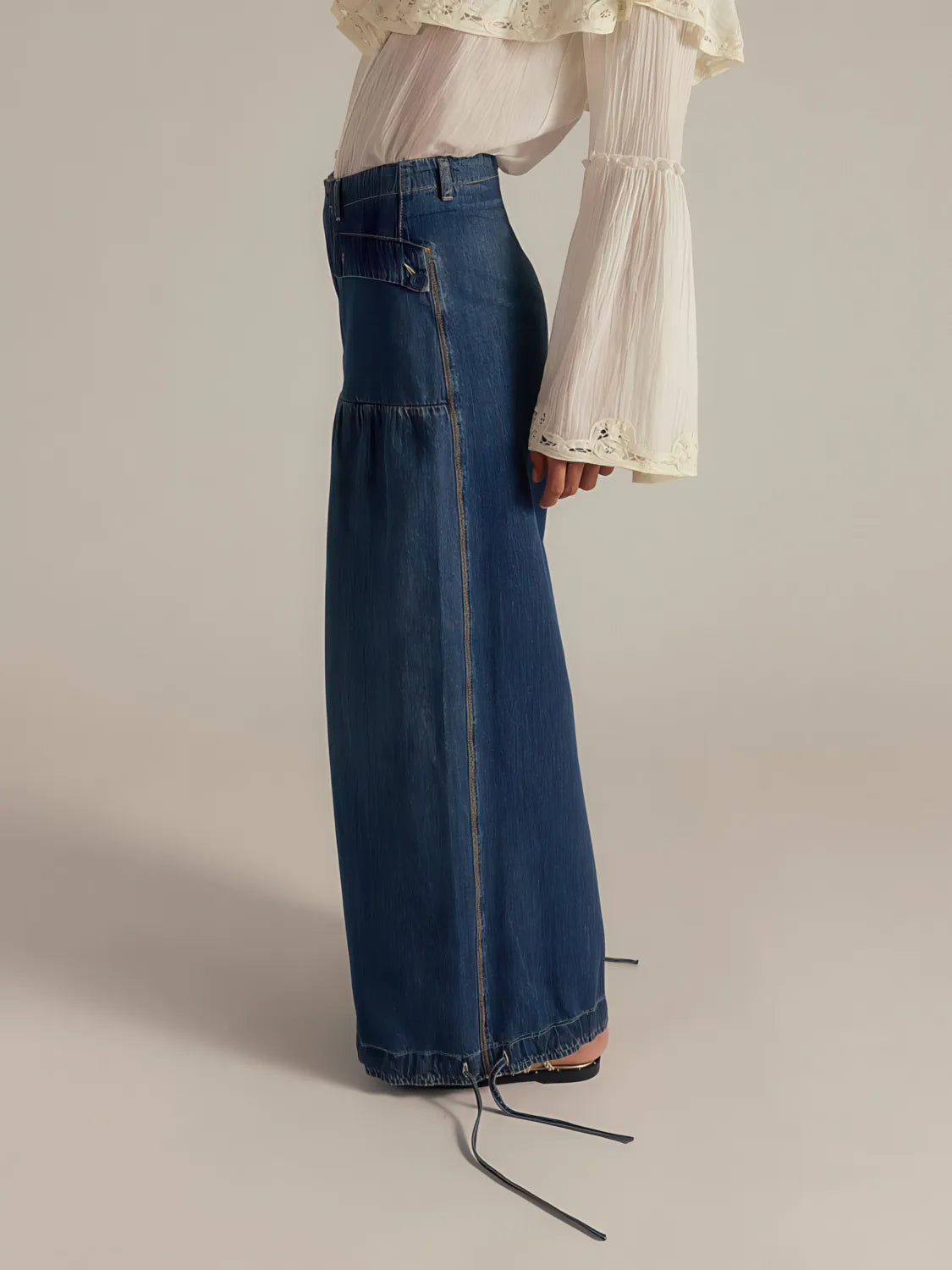 Person wearing a long blue denim skirt with a plain background. #Color_DarkBlue