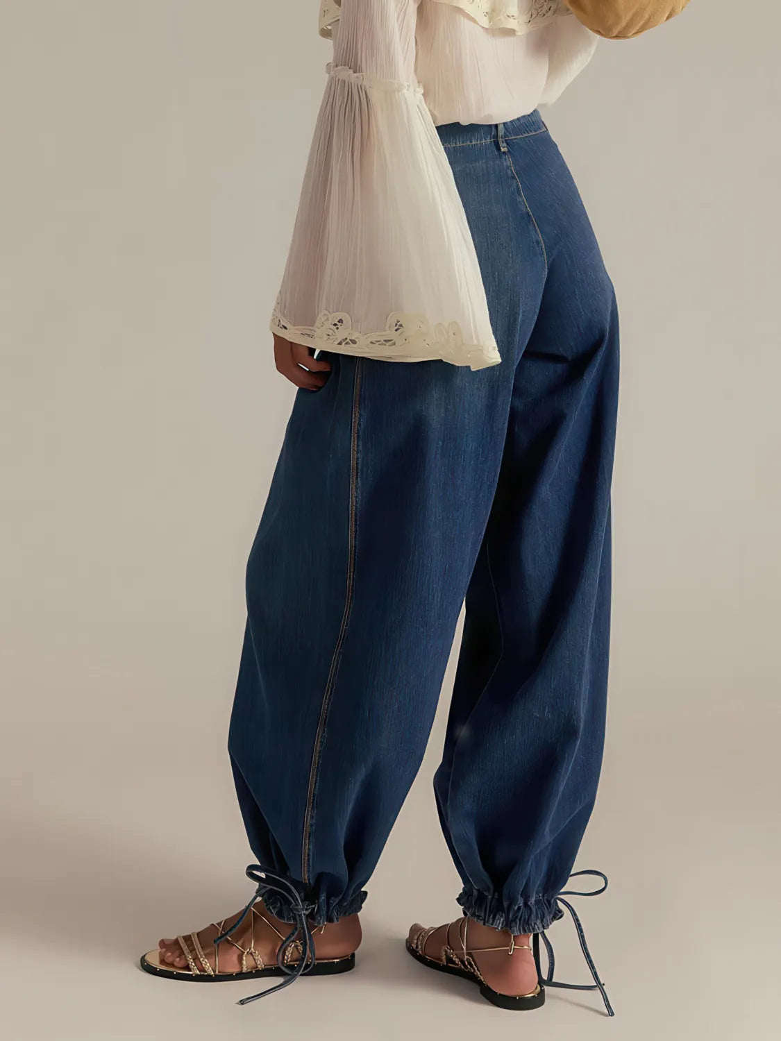 Person wearing blue jeans and a white top with a sheer overlay on a neutral background. #Color_DarkBlue