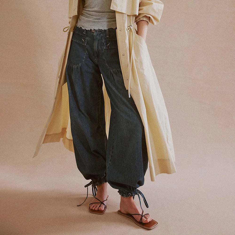 Person wearing a beige trench coat, dark jeans, and brown sandals on a plain background. #Color_DarkBlue